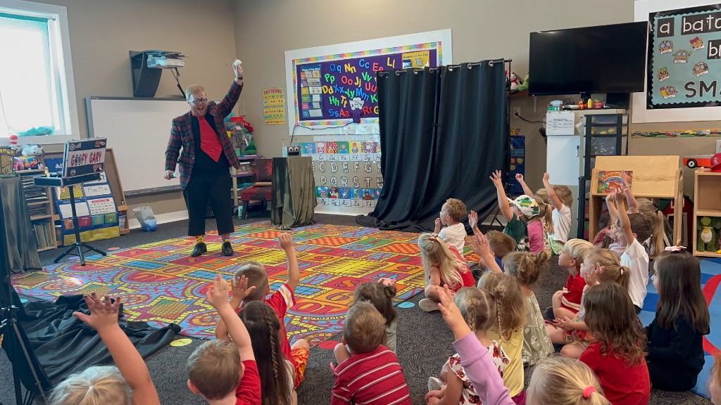 Goofy Gary performing for a room of kids with hands raised during a Kansas City magic show